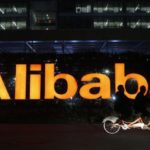 People ride a double bicycle past a logo of The Alibaba Group at the company’s headquarters on the outskirts of Hangzhou